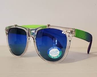 Könnte beinhalten: Transparente Plastik-Sonnenbrille mit blauen Verlaufsgläsern und einem grün-schwarz gesprenkelten Rahmen. Die Sonnenbrille hat einen Aufkleber auf der rechten Linse, auf dem "Special Lenses" und "For Beach Use" steht.