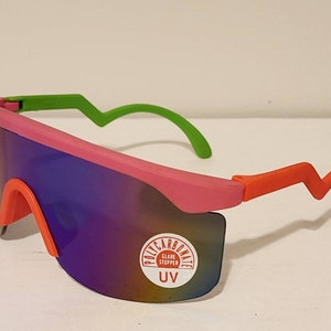 May include: Pink and orange sunglasses with green arms. The lenses are mirrored and have a sticker that says "Polycarbonate Glare Stopper UV".