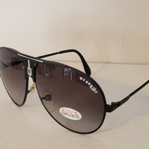 May include: Black Wrangler aviator sunglasses with gradient lenses. The sunglasses have a black frame with the Wrangler logo on the side. A UV protection sticker is visible on the lens.