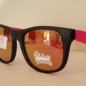 May include: Black sunglasses with pink accents and mirrored lenses. The lenses have a Teenage Mutant Ninja Turtles logo printed on them.