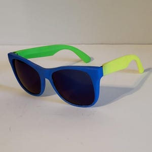May include: Blue sunglasses with dark lenses and neon green and yellow arms. The sunglasses have a classic, rectangular frame. The arms are a bright neon green and yellow, adding a pop of colour to the design. The sunglasses are a stylish accessory.