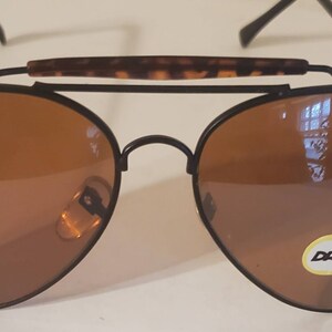 May include: Black aviator sunglasses with brown lenses and a tortoise shell brow bar. The sunglasses have a metal frame and a 'DONNA' label on the right lens.