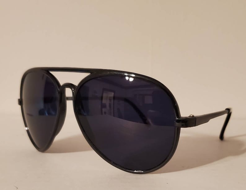 May include: Black aviator sunglasses with dark lenses. The sunglasses have a metal frame and are in focus.