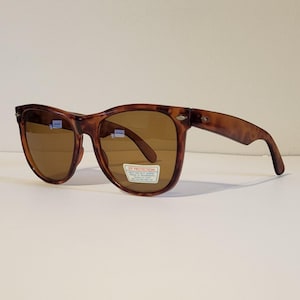 May include: Brown tortoiseshell sunglasses with brown lenses. The sunglasses have a classic rectangular frame shape. A sticker on the lens reads "UV Protection".
