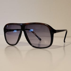 May include: Oversized sunglasses with a dark brown tortoiseshell frame and black temples. The lenses are a gradient gray color. The sunglasses have a classic aviator shape.