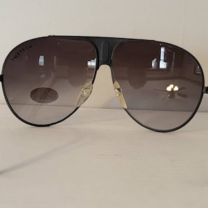 May include: Black aviator sunglasses with gradient lenses. The sunglasses have a black frame and temples. The lenses transition from a dark shade at the top to a lighter shade at the bottom. The brand name is visible on the top of the left lens.