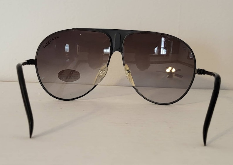 May include: Black aviator sunglasses with gradient lenses. The sunglasses have a black frame and temples. The lenses transition from a dark shade at the top to a lighter shade at the bottom. The brand name is visible on the top of the left lens.