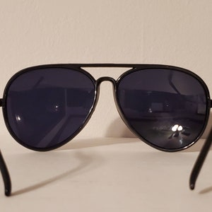 May include: Black aviator sunglasses with dark lenses. The sunglasses have a classic design with a thin metal frame.