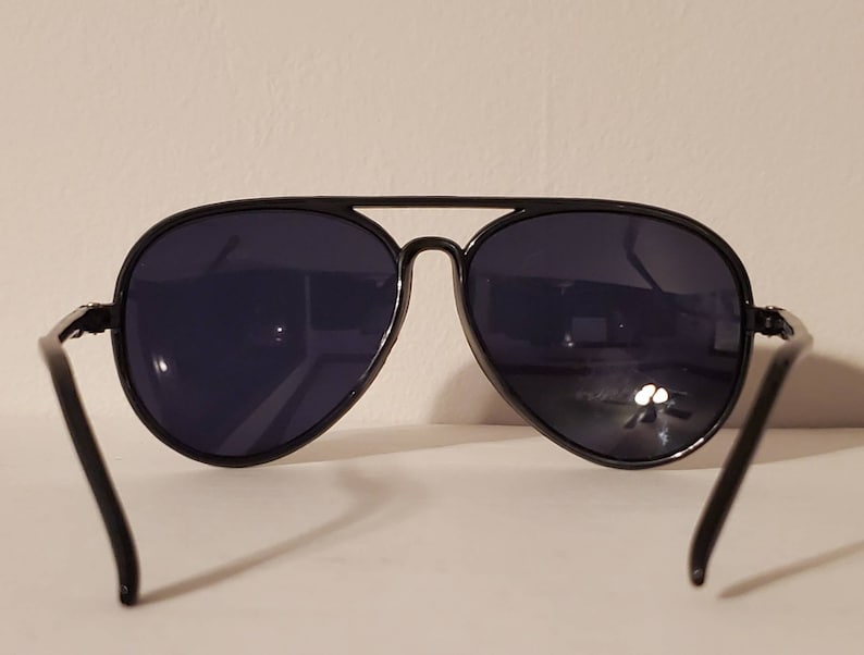 May include: Black aviator sunglasses with dark lenses. The sunglasses have a classic design with a thin metal frame.
