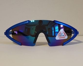 Może przedstawiać: Niebieskie okulary przeciwsłoneczne typu wraparound z lustrzanymi szkłami i czerwoną i białą etykietą z napisem "Polycarbon UV Protection Lenses".