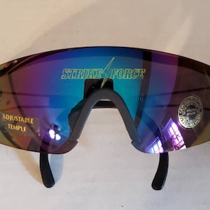 May include: Black wraparound sunglasses with iridescent lenses. The sunglasses have adjustable temples and say "STRIKE FORCE" on the lenses.