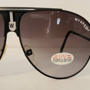May include: Black Wrangler sunglasses with gradient lenses. The sunglasses have a black frame with a white stripe and the letter "W" on the bridge. The lenses have a UV protection sticker.