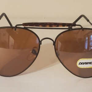May include: Brown aviator sunglasses with a black frame and a tortoise shell bridge. The sunglasses have a label that says "Donning" on the right lens.