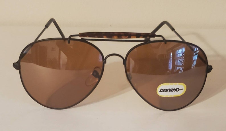 May include: Brown aviator sunglasses with a black frame and a tortoise shell bridge. The sunglasses have a label that says "Donning" on the right lens.