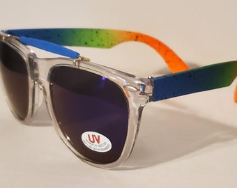 Könnte beinhalten: Transparente Sonnenbrille aus Kunststoff mit einem Regenbogen-Farbverlaufsrahmen. Der Rahmen ist blau, grün, gelb und orange. Die Gläser sind dunkelviolett und haben ein UV-Schutzlabel.