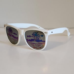 Puede incluir: Gafas de sol blancas con una escena tropical reflejada en los cristales. Las gafas de sol tienen un diseño de montura clásico. Los cristales reflejan una imagen colorida de palmeras y una playa.