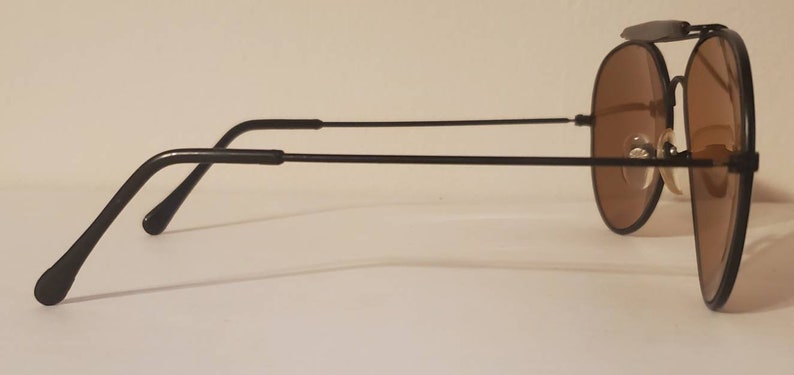 May include: Black aviator sunglasses with brown lenses. The sunglasses have a metal frame and are in a side profile view.
