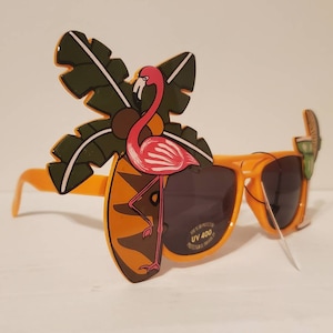 Puede incluir: Gafas de sol de plástico naranja con un diseño de flamenco rosa y palmera. Las gafas de sol tienen protección UV 400.