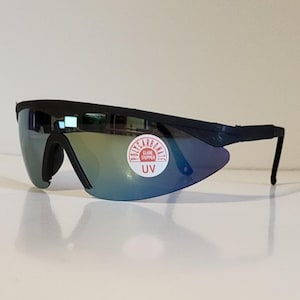 May include: Black wraparound sunglasses with a mirrored lens reflecting blue, green, and yellow. The sunglasses have a curved design and a sticker that reads "Polycarbonate, Glare Stopper, UV".