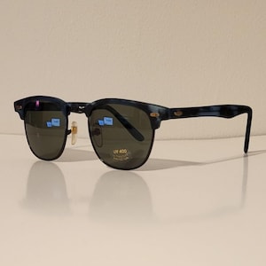 May include: Sunglasses with a dark blue frame and dark lenses. The sunglasses have a classic design with a rounded shape and a keyhole bridge. The lenses have a UV 400 protection sticker.