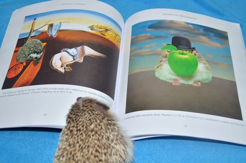 May include: An open book with two pages showing different paintings. The left page shows a painting of a melting clock and a hedgehog. The right page shows a painting of a hamster wearing a hat and holding an apple. The book is on a blue surface.