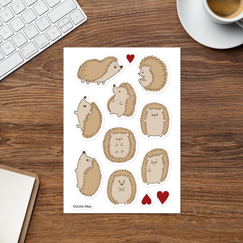 May include: A sheet of stickers featuring nine adorable cartoon hedgehogs in various poses, with two red hearts. The stickers are on a white background and have a copyright notice at the bottom that reads "&copy;Urchin Wear".