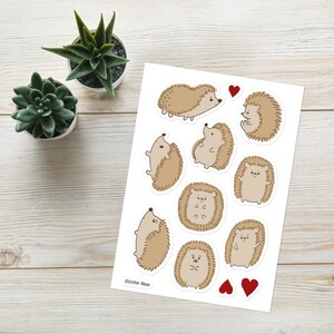 May include: A sheet of stickers featuring nine adorable cartoon hedgehogs in various poses. The hedgehogs are brown with white accents and have cute expressions. The sheet also includes two red hearts.
