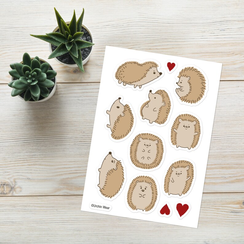 May include: A sheet of stickers featuring nine adorable cartoon hedgehogs in various poses. The hedgehogs are brown with white accents and have cute expressions. The sheet also includes two red hearts.