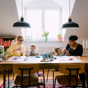 May include: A group of people are gathered around a table, working on art projects. There are paint tubes, brushes, and paper on the table. The people are all smiling and having fun.