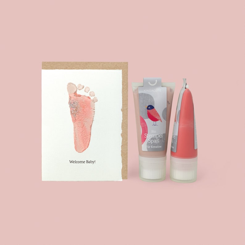 May include: A pink baby footprint on a card with the text "Welcome Baby!" and two tubes of pink paint with the text "Bio Stempel Spa&szlig; f&uuml;r Kreative" on the front.