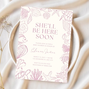 Puede incluir: Invitación a un baby shower con fondo crema y borde de criaturas marinas malva. El texto "SHE'LL BE HERE SOON" está en el centro. El texto adicional incluye la fecha, hora, lugar e información de RSVP.