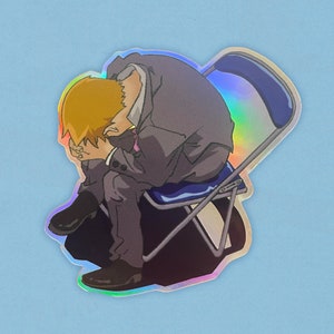 以下が含まれることがあります： 折りたたみ椅子に座って頭を手にしている漫画のキャラクターのステッカー。ステッカーはホログラフィック仕上げです。