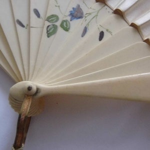 May include: A white folding fan with a floral design. The fan is closed and the handle is made of gold metal.