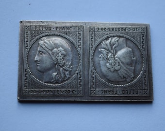 May include: A silver metal token with two sides. One side features a portrait of a woman with a crown of leaves. The other side features a design of a bird with a crown of leaves. The text "REPUB FRANC" and "20-C-POSTES-20-C" is printed on the token.