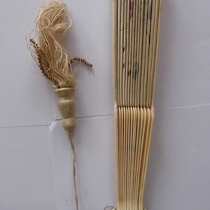 May include: A white folding fan with a tassel attached to the handle. The fan is made of ivory and has a delicate floral design.