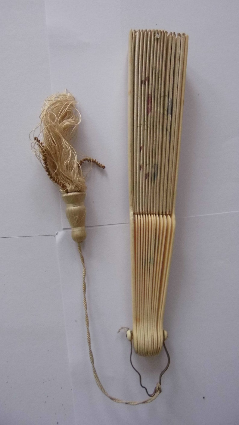May include: A white folding fan with a tassel attached to the handle. The fan is made of ivory and has a delicate floral design.