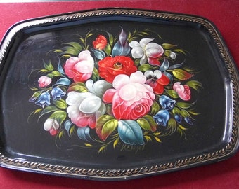 May include: A black metal tray with a gold rim and a hand-painted floral design featuring pink, red, white, and blue flowers. The tray is signed "M.Kruglova".