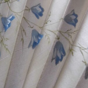 May include: A white fabric fan with a blue floral pattern. The fan is folded and has a delicate, hand-painted design.