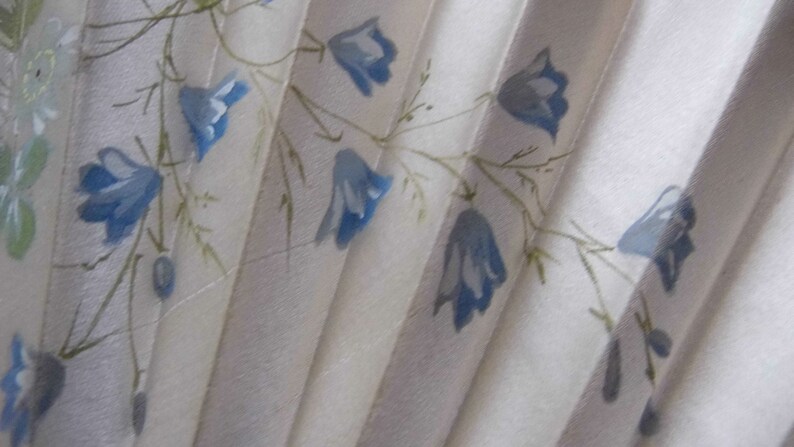 May include: A white fabric fan with a blue floral pattern. The fan is folded and has a delicate, hand-painted design.