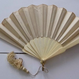 May include: A white folding fan with a cream-colored tassel. The fan is made of paper and has a wooden handle.