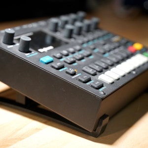 Könnte beinhalten: Ein schwarzer elektronischer Musiksynthesizer mit einer blau-weißen Tastatur und einer Vielzahl von Knöpfen und Reglern. Der Synthesizer steht auf einem schwarzen Ständer.