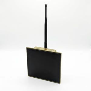 Könnte beinhalten: Ein schwarzes elektronisches Gerät mit goldfarbenem Rahmen und schwarzer Antenne. Das Gerät hat einen rechteckigen Bildschirm und einen goldfarbenen Sockel. Die Antenne ist schwarz und ragt nach oben.