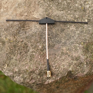 Może przedstawiać: Antena w kształcie litery T, w kolorze czarnym i miedzianym. Antena ma czarny złącze na dole i czarną plastikową podstawę.