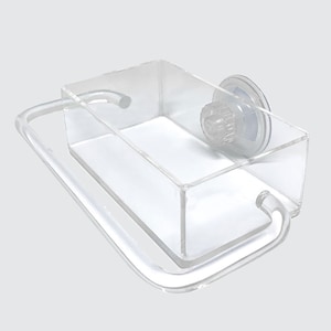 Puede incluir: Un estante de baño de acrílico transparente con un soporte de ventosa y un toallero integrado. El estante está diseñado para montarse en una superficie lisa, como una pared de ducha o un espejo.