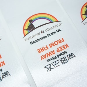 May include: White satin label with a rainbow and dinosaur logo. The text reads "rainbow & dinosaur Handmade in the UK KEEP AWAY FROM FIRE Mixed Fibres 30".