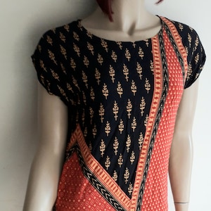 May include: A short-sleeved dress with a black and red geometric pattern. The dress has a black background with a gold floral print in the top half and a red background with a gold dot pattern in the bottom half. The dress has a black and gold trim around the neckline and hem.