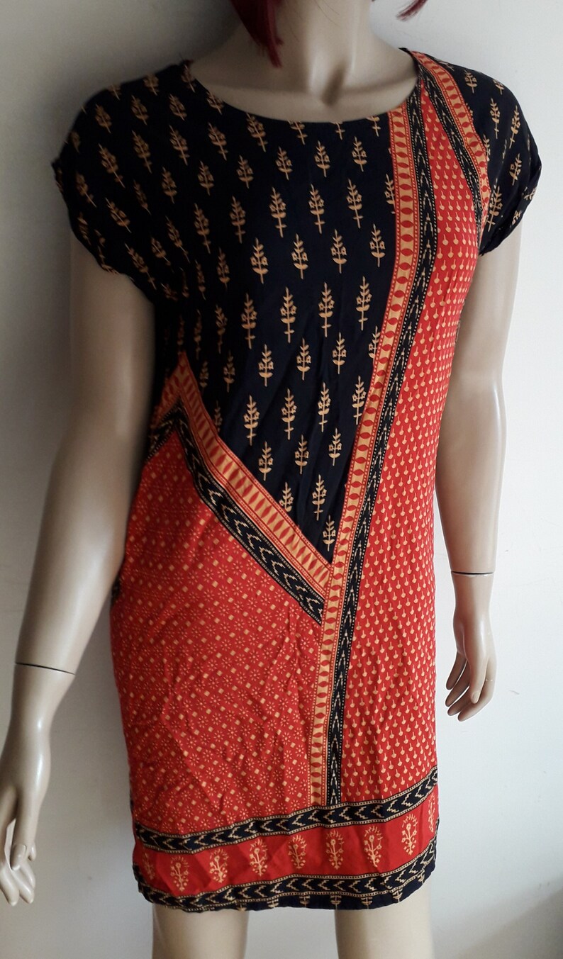 May include: A short-sleeved black and red dress with a geometric pattern. The dress has a black background with gold floral designs and a red section with a small white polka dot pattern.