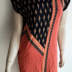 May include: A short-sleeved dress with a black and red geometric pattern. The dress has a black background with a gold floral print and a red section with a small white dot pattern. The dress has a black and gold trim.