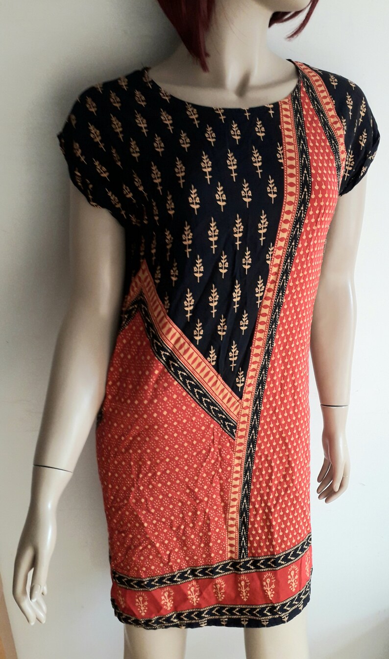 May include: A short-sleeved dress with a black and red geometric pattern. The dress has a black background with a gold floral print and a red section with a small white dot pattern. The dress has a black and gold trim.