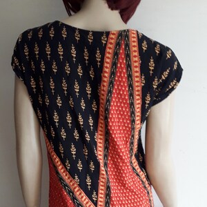 May include: A black and red dress with a geometric pattern and gold accents. The dress has short sleeves and a scoop neck.